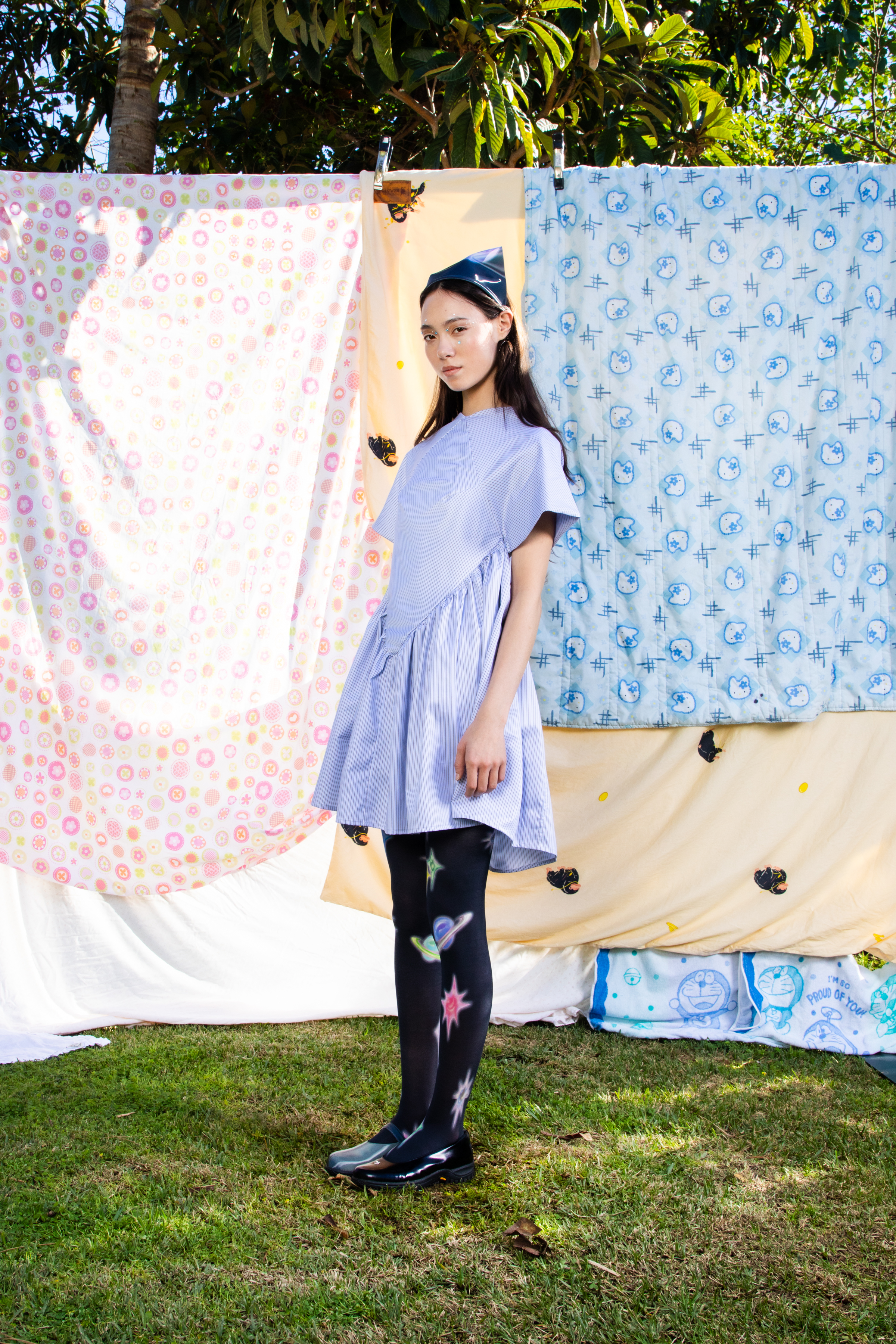 Full body shot of female model in a blue dres and black galaxy print leggings against a backdrop of patterned quilts.